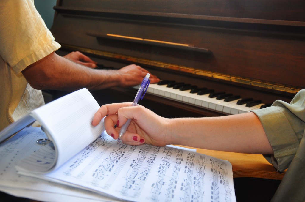 יד כותבת תווים ומאחורה ידיים מנגנות על פסנתר