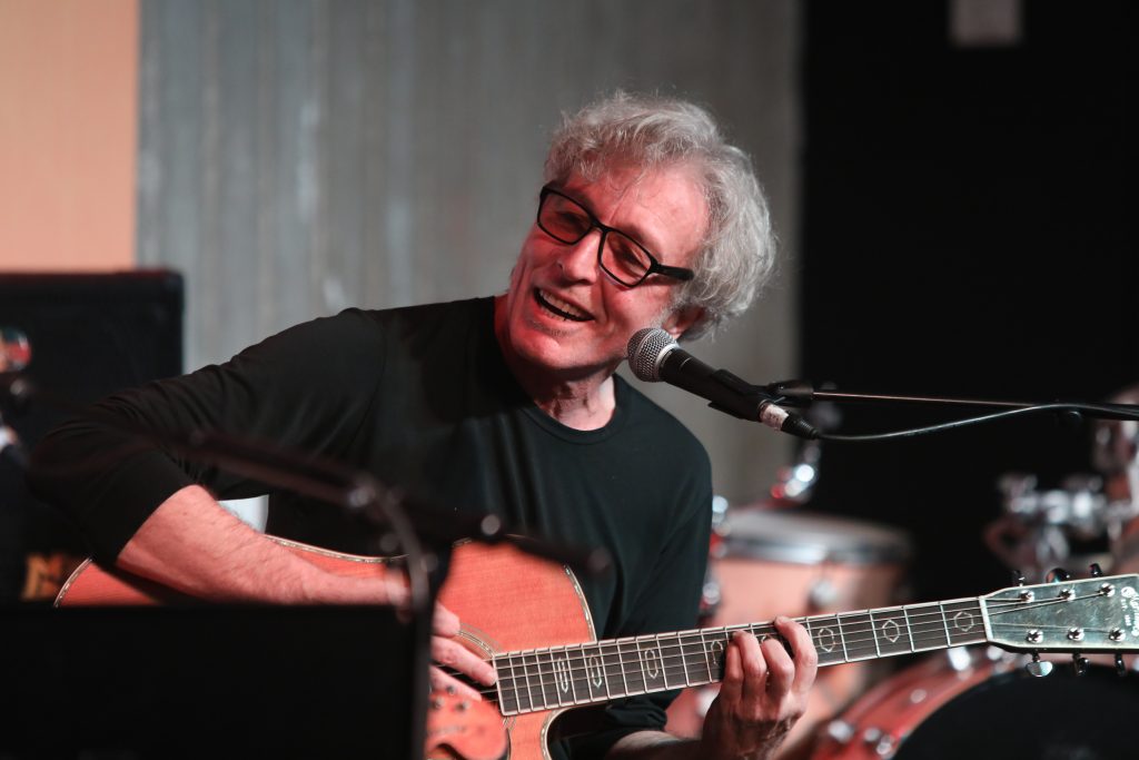 מורה לגיטרה עם גיטרה ביד מחייך לצד