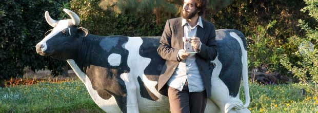 המרצה ימי ויסלר שותה קפה ונשען על פסל של פרה